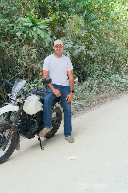 Corpo inteiro de jovem motociclista étnico hispânico sério em roupas casuais e boné em pé na motocicleta
