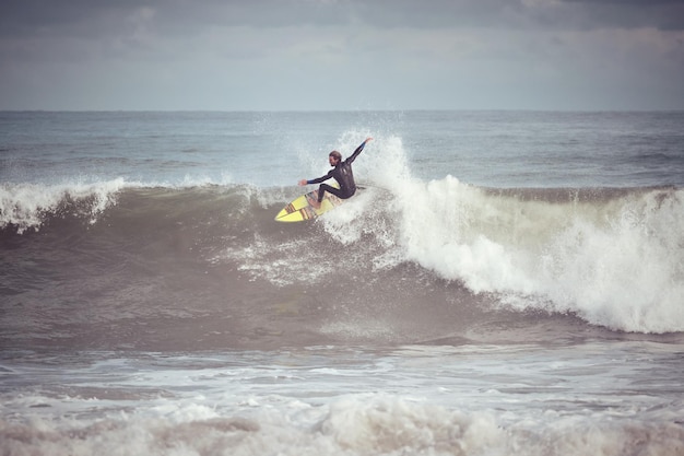 Corpo inteiro de surfista masculino em pé na prancha pegando onda e andando na onda enquanto desfruta de um hobby extremo no oceano