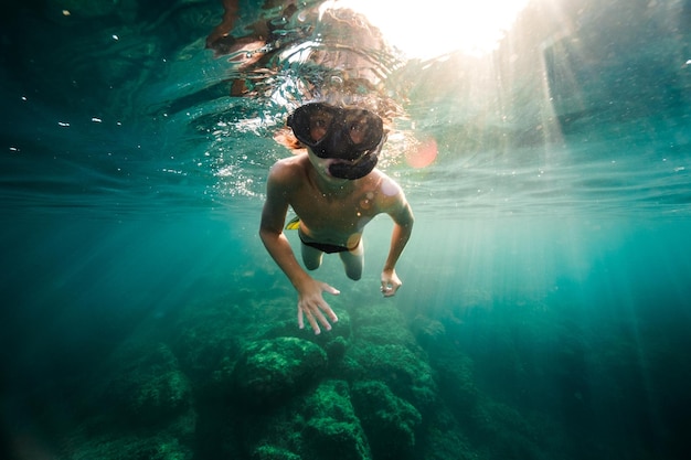 Corpo inteiro do jovem mergulhador sem camisa em máscara de mergulho explorando o oceano azul durante o mergulho em dia ensolarado