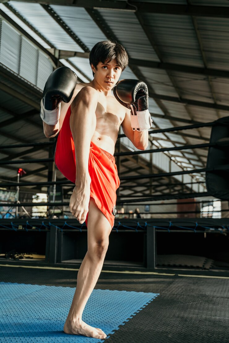 Foto corpo inteiro do melhor lutador em luvas de boxe com chute no joelho em pé na arena do ringue