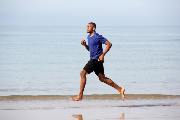 Corpo inteiro jovem macho Africano correndo ao longo da costa do mar