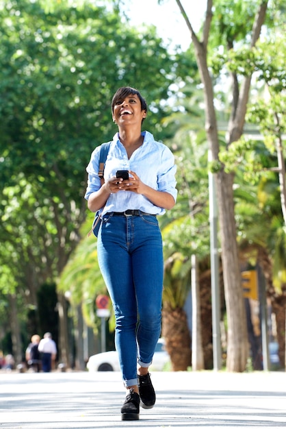 Corpo inteiro, jovem, senhora preta, andar, com, telefone móvel, exterior