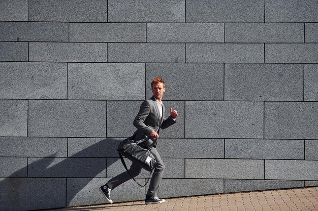 Corre y llega al trabajo El joven hombre de negocios con ropa formal gris está al aire libre en la ciudad