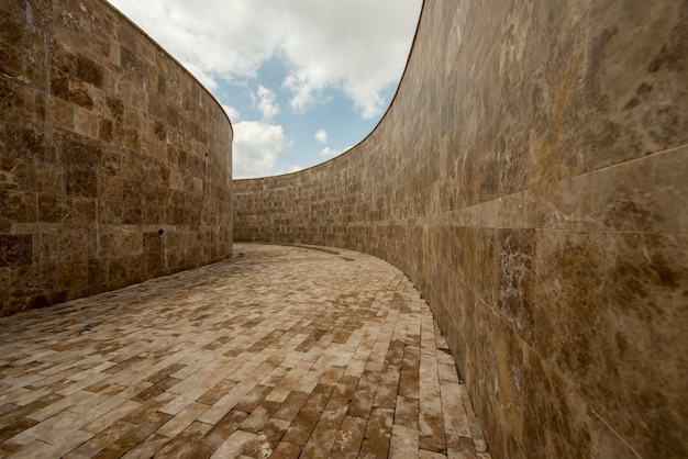 Corredor con altos muros curvos revestidos de baldosas de mármol marrón y suelo empedrado Arquitectura exterior