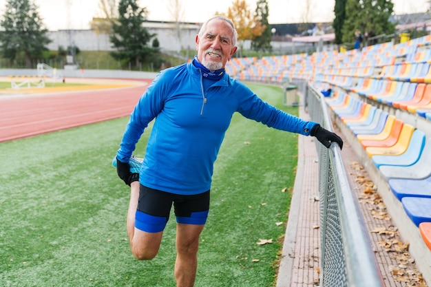 Foto corredor caucasiano sênior alegre se estende em uma pista vazia do estádio mostrando um estilo de vida ativo