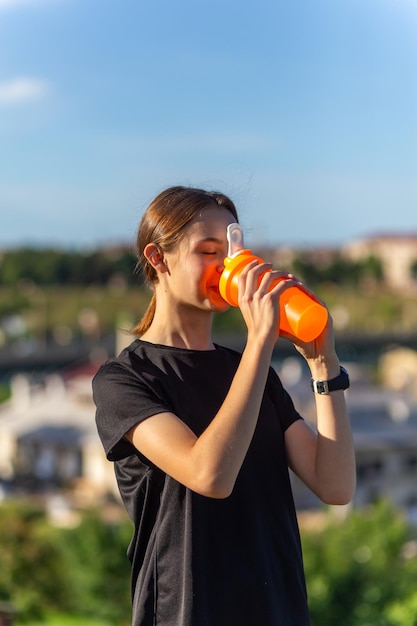 Corredor de chica tennage en forma al aire libre sosteniendo una botella de agua Mujer de fitness tomando un descanso después de hacer ejercicio