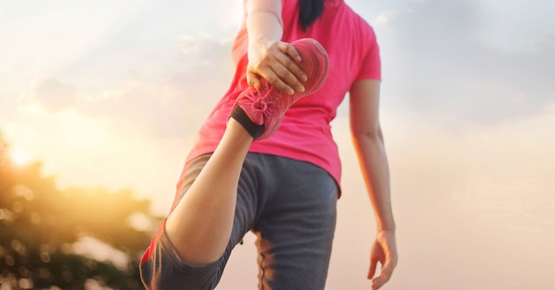 Foto corredor da jovem mulher que estica os pés antes de correr na fuga rural do por do sol.