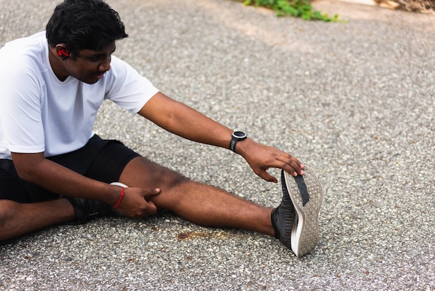 Corredor de esporte homem negro usar relógio ele sentado puxar os dedos dos pés, esticando as pernas e joelho