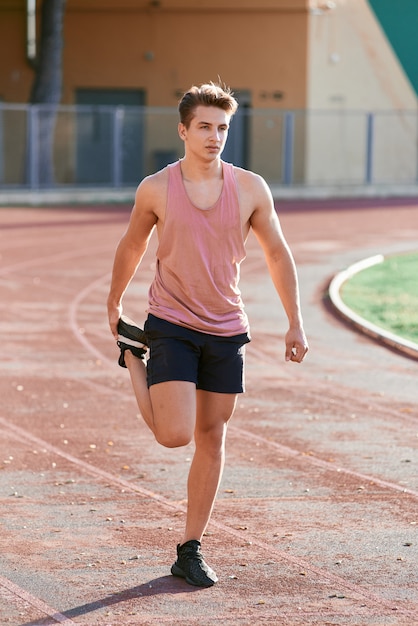 Corredor de jovem esticando a perna na pista de corrida no estádio