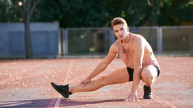 Corredor de jovem esticando a perna na pista de corrida no estádio