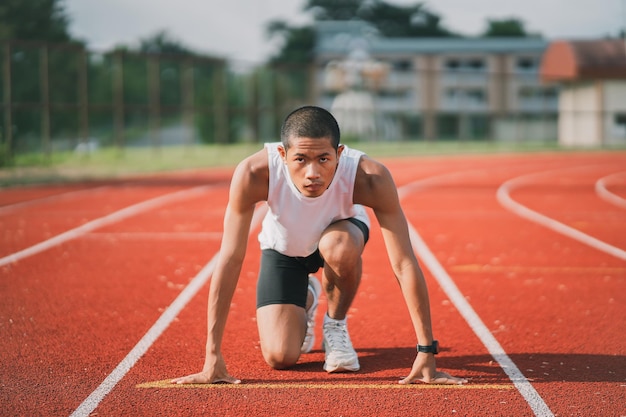 Corredor de mãos pronto para começar a correr o treinamento do atleta esportista correr na pista no estádio de manhã homem corredor vestindo colete branco para praticar corrida preparar-se para a corrida de competição