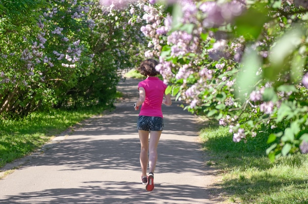 Corredor de mulher correndo no parque primavera com flor lilás, manhã correr ao ar livre, fitness e executando o conceito de estilo de vida saudável