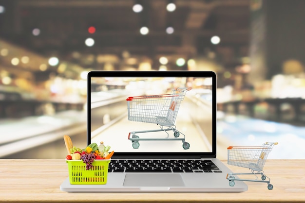 Corredor de supermercado desfocado fundo com computador laptop e carrinho de compras no conceito online de mercearia de mesa de madeira
