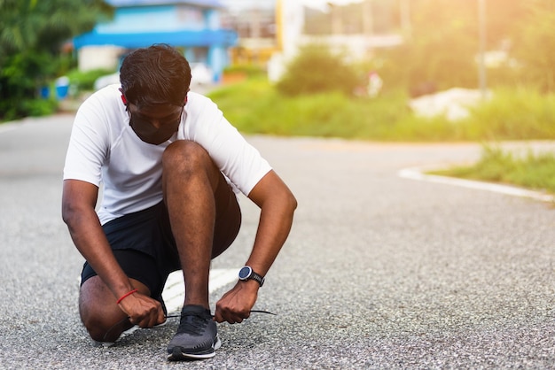 Corredor deportivo asiático de cerca hombre negro usar reloj sentado él tratando cordón de zapatos para correr preparándose para correr y correr al aire libre calle parque de salud con espacio de copia concepto de entrenamiento de ejercicio saludable