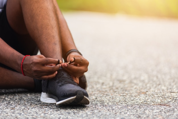 Corredor deportivo hombre negro sentado cordones tratando de zapatillas preparándose para trotar