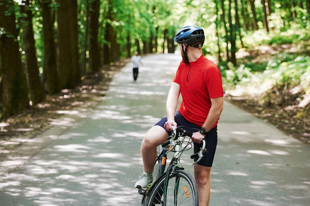 Corredor detrás. Ciclista en bicicleta está en la carretera asfaltada en el bosque en día soleado