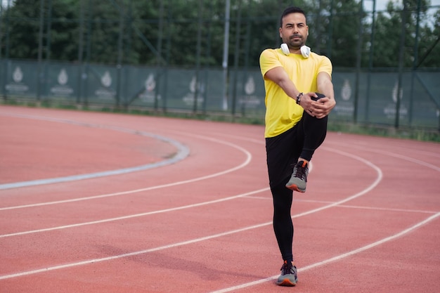 Corredor dinâmico com fones de ouvido sem fio flexiona os músculos das pernas em pista de corrida de borracha