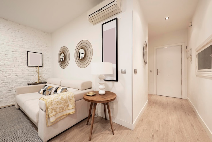 Foto corredor e sala de estar com sofá de tecido branco e mesa lateral redonda de madeira em casa de aluguel por temporada