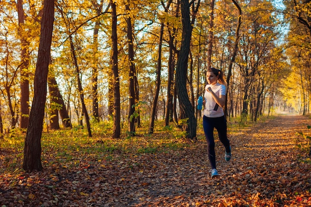 Corredor ejercicio en otoño parque. Mujer que corre con la botella de agua al atardecer. Estilo de vida activo