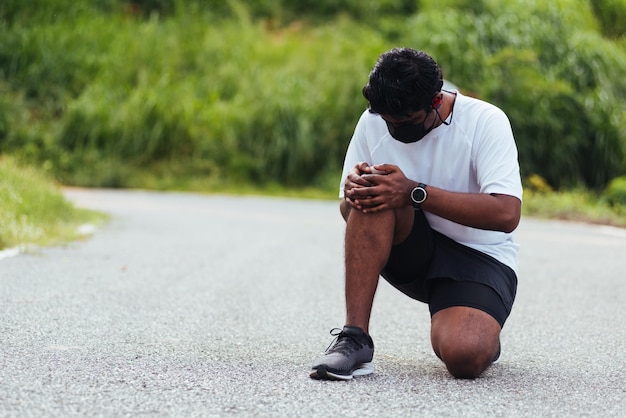 Foto corredor esportivo homem negro usa relógio sentado mãos juntas segura joelho