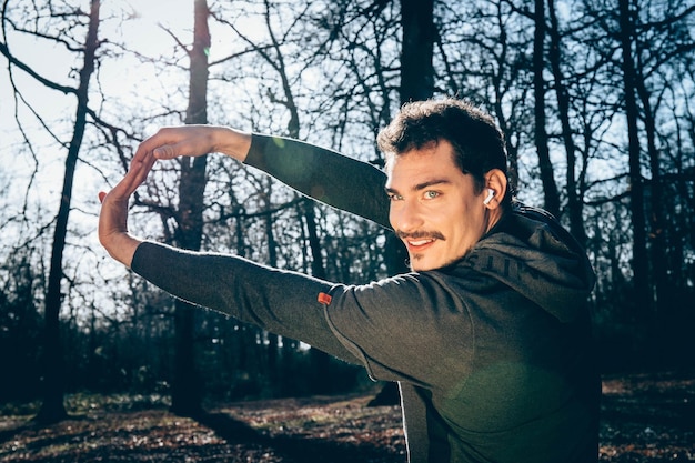El corredor se está estirando en el bosque el hombre de ojos azules y bigote está entrenando en el parque
