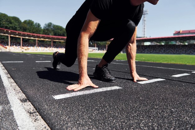 El corredor está en la posición inicial en la pista Un joven deportivo con camisa negra y pantalones al aire libre durante el día