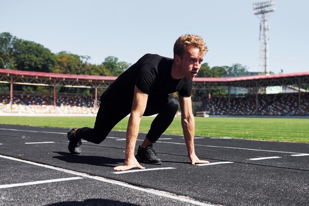 El corredor está en la posición inicial en la pista Un joven deportivo con camisa negra y pantalones al aire libre durante el día