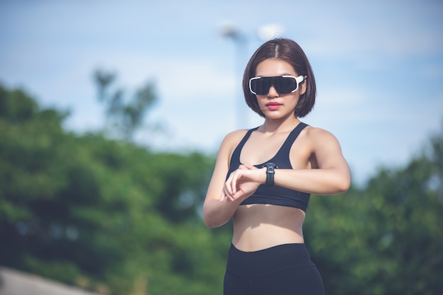 Corredor femenino comprobando reloj inteligente rastreador de ejercicios y sonriendo después de correr y correr piernas