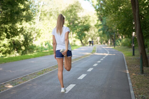 Corredor feminino esticando as pernas antes de se exercitar no parque de verão.