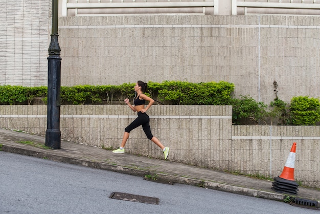 Corredor feminino, subindo a colina na rua da cidade. Desportiva jovem fazendo cardio- exercícios ao ar livre.