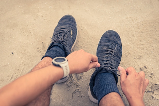 Corredor hombre atar cordones de los zapatos listos para correr en la playa