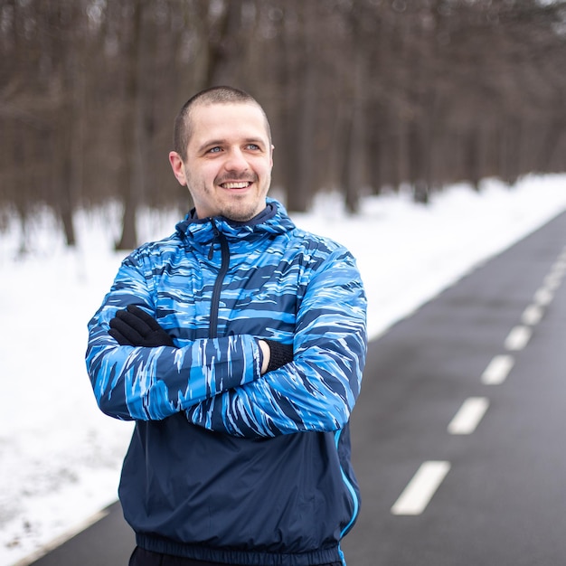 Corredor de hombre deportivo mirando de lado y sonriendo de pie en la pista de atletismo de invierno