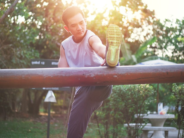 Foto corredor joven asiático haciendo ejercicio de estiramiento, preparándose para el entrenamiento de la mañana en el parque