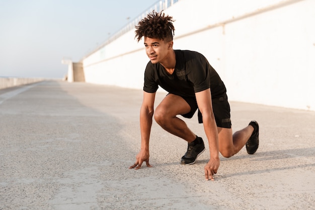 Corredor joven deportista de pie listo para comenzar al aire libre en la playa