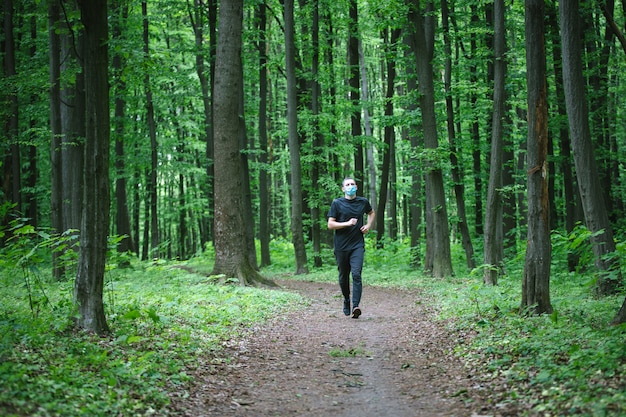 Corredor con máscara médica. Pandemia de coronavirus Covid-19 un hombre con una máscara médica corre en el bosque