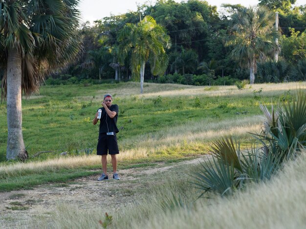 Corredor masculino água potável fora da garrafa de plástico após treino cardio, usando fones de ouvido brancos. esportista no sportswear preto, hidratante durante o treinamento ao ar livre.