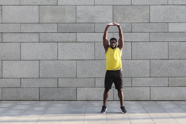 Corredor masculino em roupa esportiva amarela alongando-se antes de fazer exercícios matinais