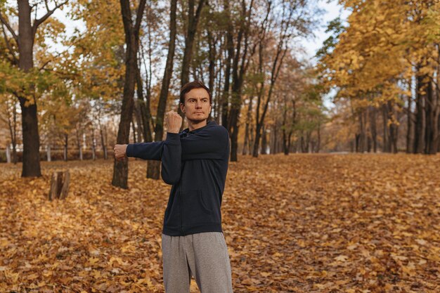 Corredor masculino sério em roupas ativas aquecendo os braços e alongando o corpo durante o treino