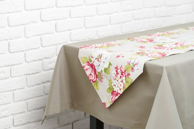 Corredor de mesa floral en un mantel de mesa beige contra una pared de ladrillo blanco