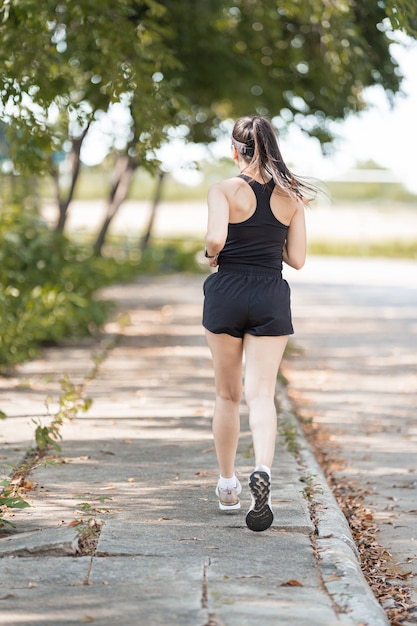 Un corredor de mujer asiática feliz saludable en trajes deportivos negros trotar en el parque natural de la ciudad bajo el atardecer de la tarde