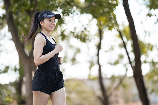 Un corredor de mujer asiática feliz saludable en trajes deportivos negros trotar en el parque natural de la ciudad bajo el atardecer de la tarde