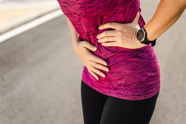 Corredor de la mujer que tiene calambres de estómago después de correr Jogging