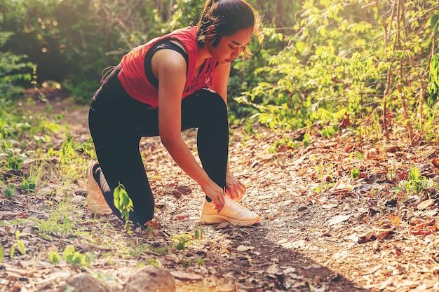 Corredor de la mujer en el sendero del bosque atando sus zapatos preparándose para entrenar al aire libre