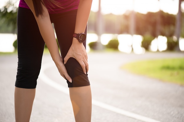 El corredor de la mujer siente dolor en su rodilla en el parque.