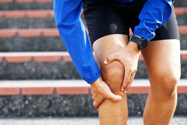 Corredor tocando doloroso retorcido o roto. Entrenamiento de atletas, subiendo y bajando escaleras por accidente. El esguince deportivo causa lesión de rodilla. y dolor en los huesos de las piernas.