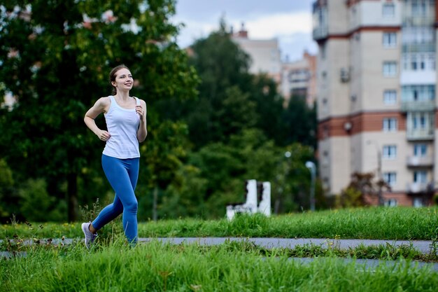 La corredora con camiseta blanca y polainas está trotando en una zona residencial el día de verano