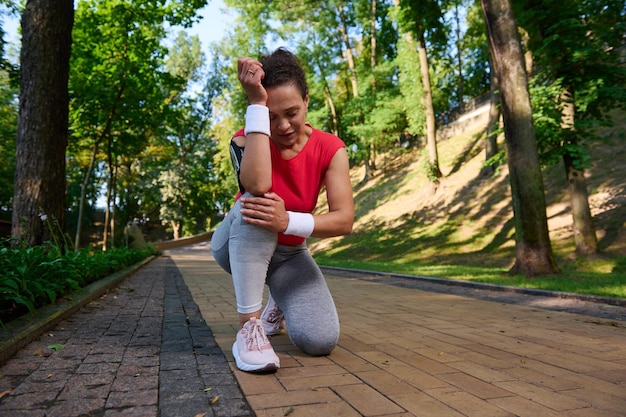 La corredora deportista exhausta siente dolor en la rodilla mientras corre por un sendero en un parque forestal Lesión deportiva Dolor en la rodilla Concepto deportivo