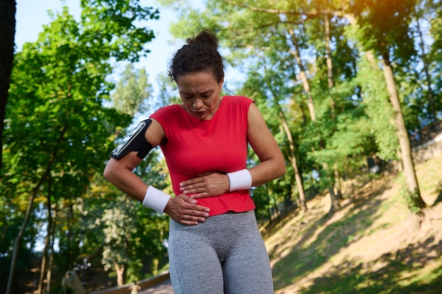 La corredora deportista que se sujeta el estómago siente dolores punzantes en el costado mientras trota Concepto de salud y lesiones deportivas