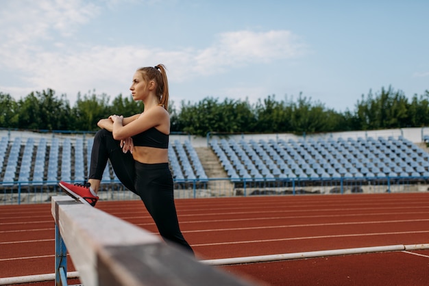 Corredoras en ropa deportiva, ejercicios de estiramiento en el estadio. Mujer delgada haciendo ejercicio antes de correr en la arena al aire libre