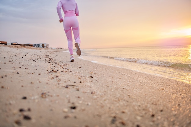 Corredoras en traje deportivo rosa realizando jog en la playa temprano en la mañana